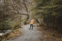 Rückansicht eines männlichen Reisenden in leuchtend orangefarbener Jacke, der an einem Frühlingstag den Weg neben der alten Steinbrücke beim Besuch des Tollymore Forest Park in Nordirland beschreitet — Stockfoto