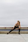 Mulher esportiva motivada no desgaste ativo em pé e pernas esticadas enquanto olha para longe — Fotografia de Stock