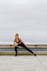 Femme sportive motivée dans l'usure active debout étirant les jambes tout en regardant loin — Photo de stock