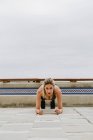 Athlète féminine concentrée en tenue active élégante faisant de la planche sur une plage de sable vide le jour couvert — Photo de stock