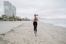 Visão traseira da mulher em forma correndo ao longo da costa tropical vazia em tempo nublado — Fotografia de Stock