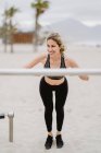 Мотивированная спортивная женщина в активном износе тренируется в металлическом баре на песчаном пляже — стоковое фото