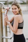Mulher esportiva motivada em uso ativo segurando barra de metal enquanto descansa na praia — Fotografia de Stock