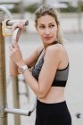 Мотивована спортивна жінка в активному носінні тримає металевий бар під час відпочинку на піщаному пляжі — стокове фото