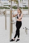 Vue latérale de la femme sportive motivée en tenue active tenant barre métallique tout en se reposant à la plage de sable fin — Photo de stock