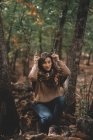 Mulher engraçada em roupa casual segurando varas como chifres e olhando para longe enquanto sentado em pedra na floresta — Fotografia de Stock
