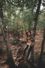 Calme jeune femme en chapeau élégant et écharpe debout dans la forêt d'automne regardant loin tout en se reposant dans la forêt verte — Photo de stock