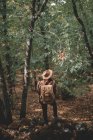 Vue arrière de la femme anonyme avec chapeau ajustable sac à dos tout en voyageant à travers la forêt verte dans la nature — Photo de stock