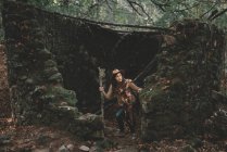 Mulher com pau de madeira explorando velhas ruínas na floresta verde na natureza — Fotografia de Stock