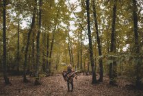 Visão traseira de uma jovem mulher irreconhecível em chapéu embrulhando em cachecol quadriculado enquanto estava em pé em folhas secas na floresta de outono — Fotografia de Stock