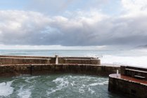 Landscape of fenced with stone walls water and wavy blue sea with cloudy sky on background at Zarautz at Spain — Stock Photo