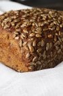 Loaf of grainy organic bread with seeds on white towel — Stock Photo