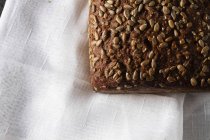 Loaf of grainy organic bread with seeds on white towel — Stock Photo