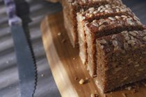 Нарезанный цельнозерновой хлеб на деревянной доске с ножом — стоковое фото