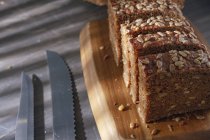 Нарезанный цельнозерновой хлеб на деревянной доске с ножами — стоковое фото