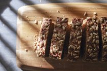 Pão integral fatiado em tábua de corte de madeira na mesa com sombra — Fotografia de Stock