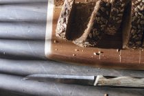 Geschnittenes Vollkornbrot auf Holzschneidebrett auf Tisch mit Schatten — Stockfoto