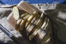 Draufsicht auf servierte frische Brotscheiben auf Schneidebrett mit Messer auf Leinwand-Serviette — Stockfoto