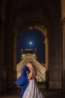 Jovem casal recém-casado em terno de casamento e vestido abraçando enquanto estava em pé em arco balançado com Louvre no fundo em Paris — Fotografia de Stock