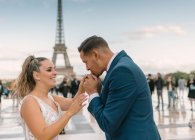Groom in blue suit and bride in white wedding gown kissing hand with Eiffel Tower on background at Paris — Stock Photo