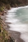 Desde arriba, una costa tranquila y pintoresca con tranquilas olas de arena a la luz del sol en la playa rocosa de Silence O Gaviero. - foto de stock