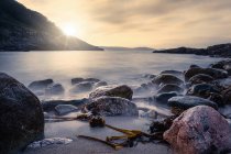 Туманная поверхность моря с большими скалами на песчаном пляже и горы на восходе солнца на пляже Портоново в Италии — стоковое фото
