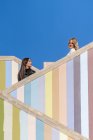 Side view of attractive pensive young friends in jackets standing on different level of striped colored stairs outdoors — Stock Photo
