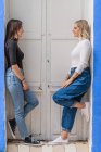 Side view of happy gentle caring girlfriends in stylish outfit standing near door looking at each other — Stock Photo