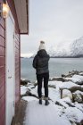 Mulher solitária na costa rochosa contra o lago tranquilo e montanhas nevadas no dia frio — Fotografia de Stock