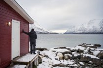 Einsamer Mann am felsigen Ufer gegen ruhigen See und verschneites Gebirge — Stockfoto