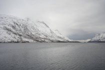 Ruhiger See vor verschneiten Hügeln bei kaltem, bewölktem Wetter — Stockfoto