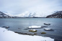 Lago tranquilo contra colinas nevadas em tempo nublado frio — Fotografia de Stock