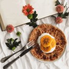 Top view of homemade crepes with cream and sliced persimmon served on plate with knife and fork on surface decorated with white cloth and flowers next to open book with empty pages — Stock Photo