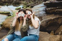Молодые путешественницы сидят на камне и закрывают глаза цветами — стоковое фото