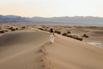 Vue arrière de la jeune femme marchant dans le désert laissant des empreintes de pas dans — Photo de stock