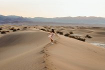 Vue arrière de la jeune femme marchant dans le désert laissant des empreintes de pas dans — Photo de stock