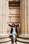 Mujer apoyada en el pavimento entre altas columnas masivas y miradas - foto de stock