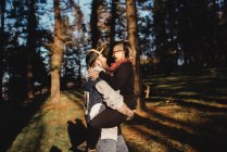 Side view of bearded man holding on hands cheerful young lady and going in forest on blurred background — Stock Photo