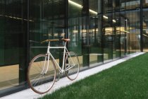 Bicicleta aparcada en la acera cerca de la pared del edificio contemporáneo en el día soleado en la calle de la ciudad - foto de stock