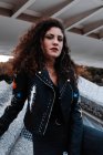 Mujer moderna en chaqueta negra y jeans de pie en la ciudad - foto de stock