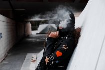Donna in maschera nera e giacca che fuma per strada — Foto stock
