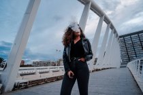 Mulher elegante em casaco preto e jeans fumando na ponte — Fotografia de Stock