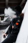 Жінка в чорній масці і куртці курить на вулиці — стокове фото