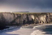 Impresionante paisaje marino de la costa de Irlanda del Norte con rocas y hierba verde de primavera y olas tormentosas del océano frío rompiendo en la orilla con espuma - foto de stock