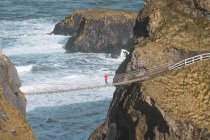 Tourist walking on rope bridge suspended between cliffs in Northern Ireland — Stock Photo