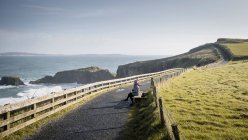 Donna seduta su panchina su strada di campagna tra mare e campo — Foto stock