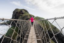 Mulher atravessando ponte corda levando a ilha rochosa — Fotografia de Stock