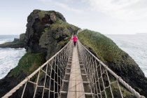 Femme traversant pont de corde menant à l'île rocheuse — Photo de stock