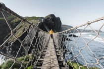 Hombre cruzando el puente de cuerda que conduce a la isla rocosa - foto de stock