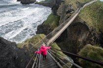 Mulher atravessando ponte corda levando a ilha rochosa — Fotografia de Stock
